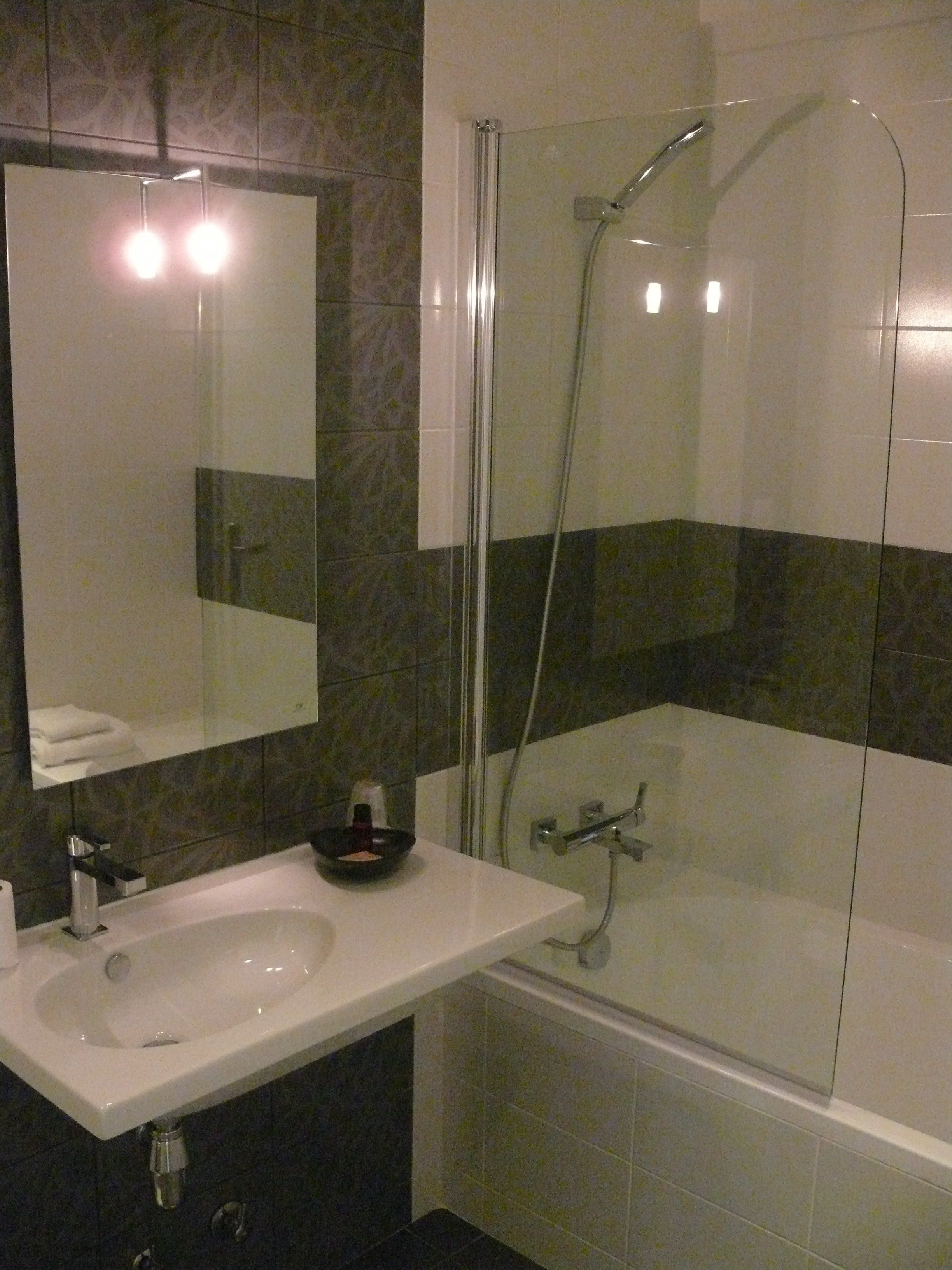 Een badkamer met een douche met glazen wand, een wastafel en een spiegel.