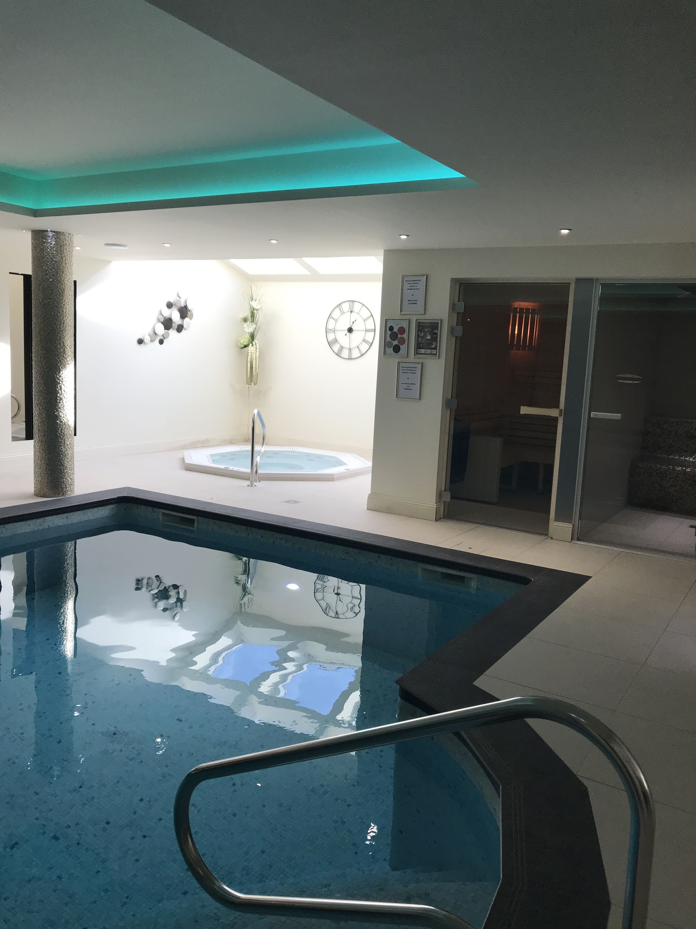 An indoor swimming pool with a clear view of the surrounding area, including a clock, framed pictures, and a door leading to another room.
