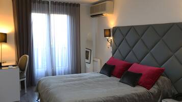 A hotel room with a bed, a desk, a chair, an air conditioning unit, and a window with curtains.
