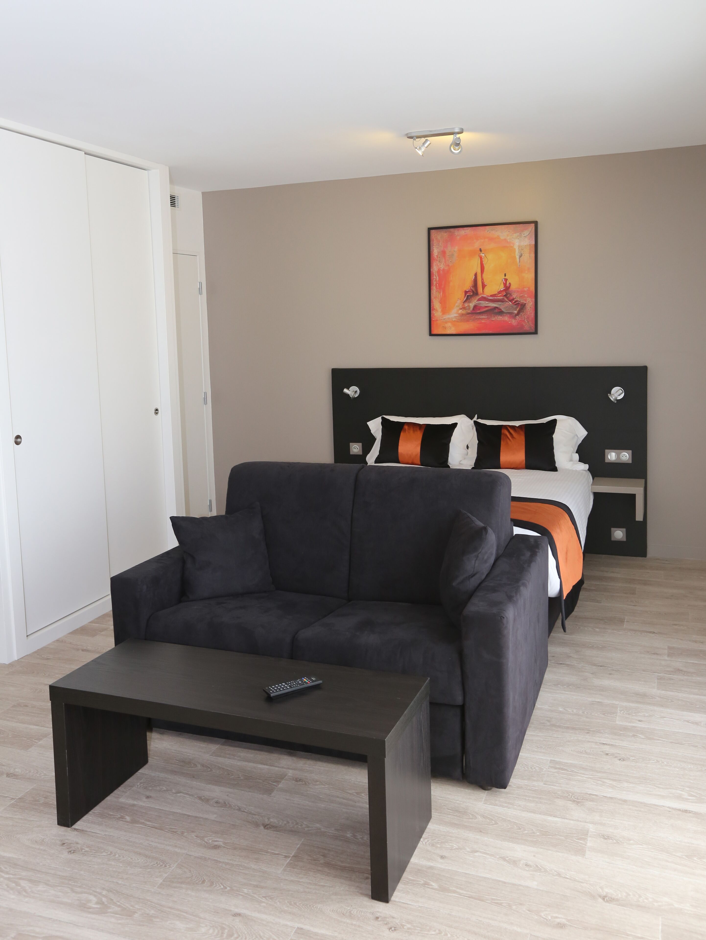 A modern hotel room with a dark sofa, a small coffee table, and a bed with a black headboard.