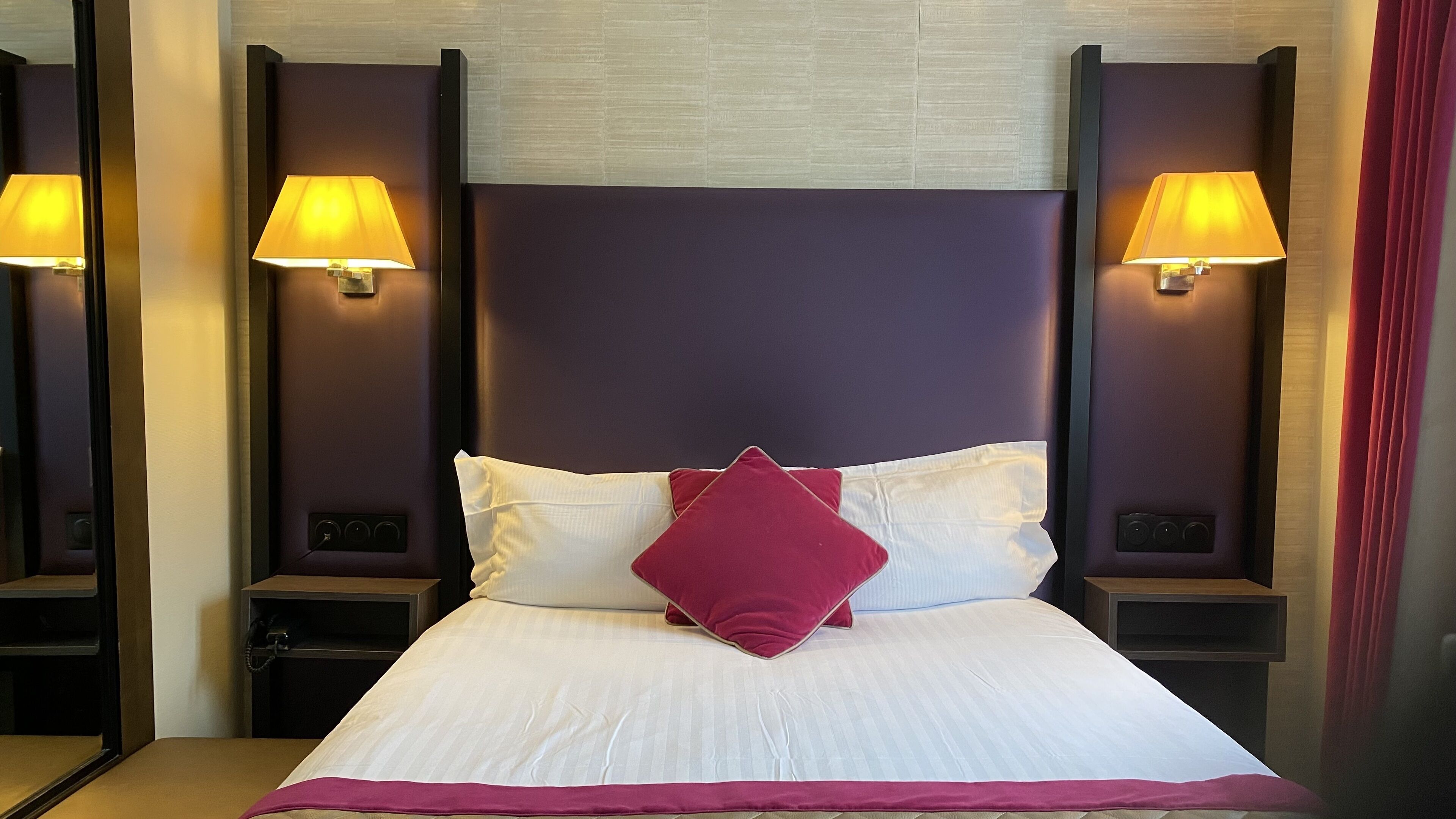 A hotel room with a large bed, two bedside lamps, and a headboard.