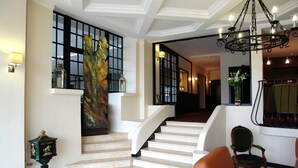 A grand staircase with a decorative wall piece, a vintage lantern, and a modern chandelier. - Hôtel Bellevue (Amboise)