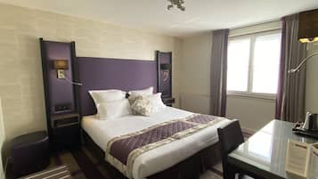 A hotel room with a large bed, a desk, and a window with curtains.