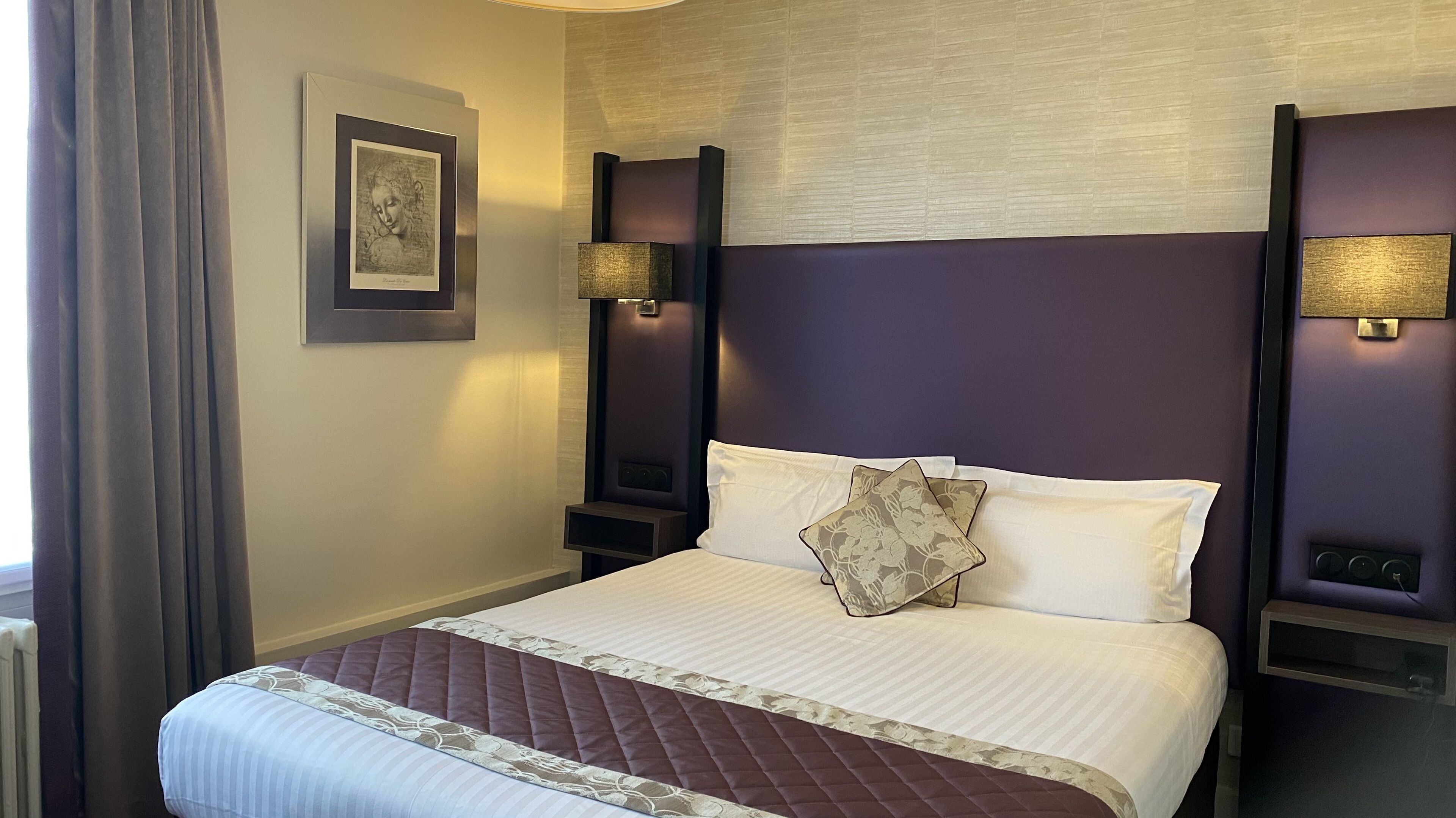 Habitación de hotel con una cama grande, dos mesitas de noche, una obra de arte enmarcada en la pared y una ventana con cortinas.