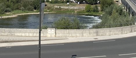 Un río con un puente de piedra, un edificio blanco y una calle con coches.