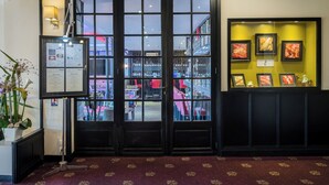 A hotel lobby with a reception desk, a glass door entrance, and a wall with framed artwork. - Hôtel Bellevue (Amboise)