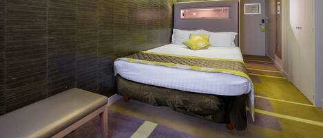 A hotel room with a bed, bench, and a wall with a textured pattern.