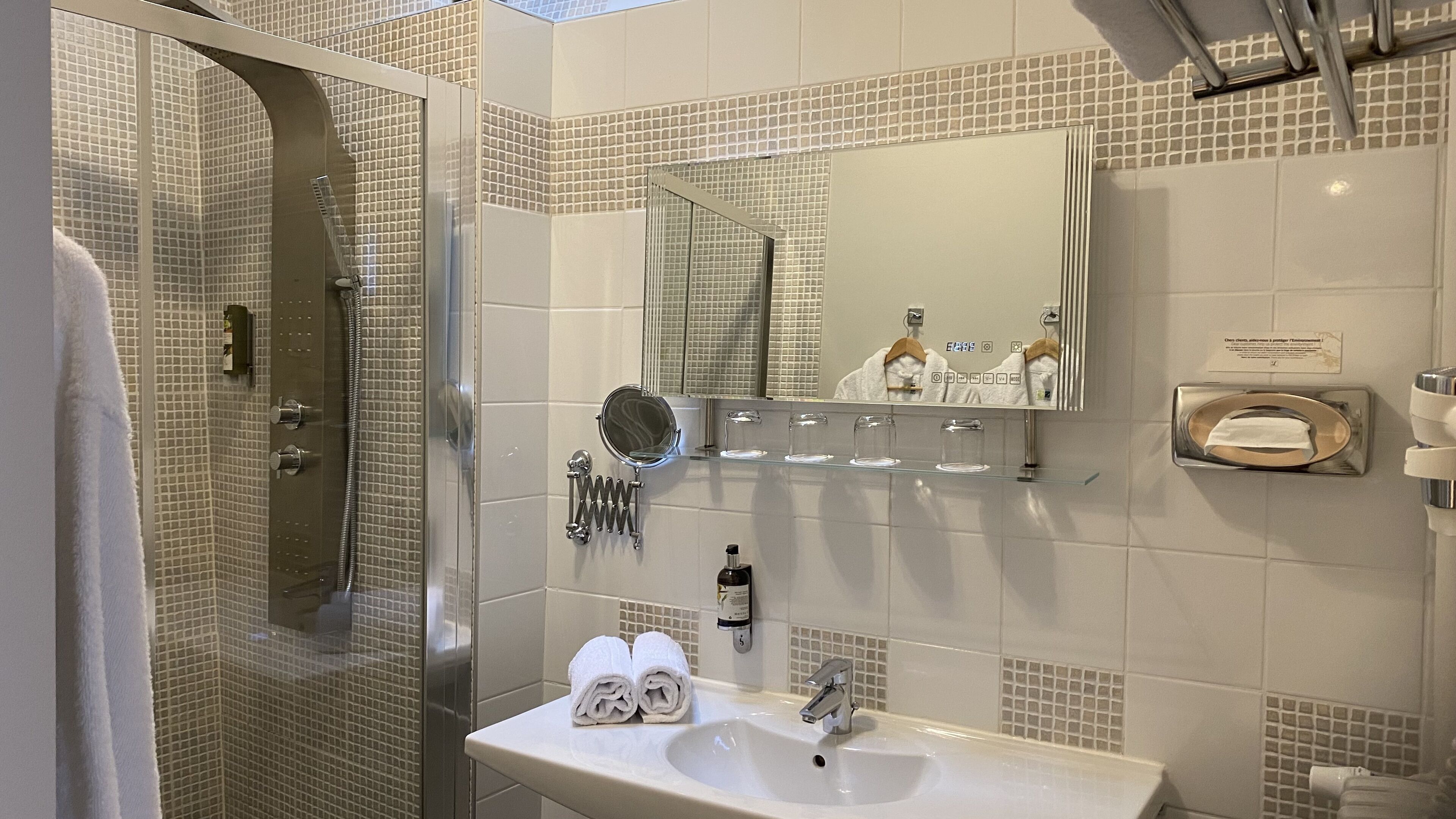 Un baño moderno con ducha envuelta en vidrio, un lavamanos con espejo y un perchero con toallas.