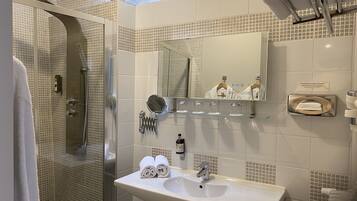 Un baño moderno con ducha envuelta en vidrio, un lavamanos con espejo y un perchero con toallas.