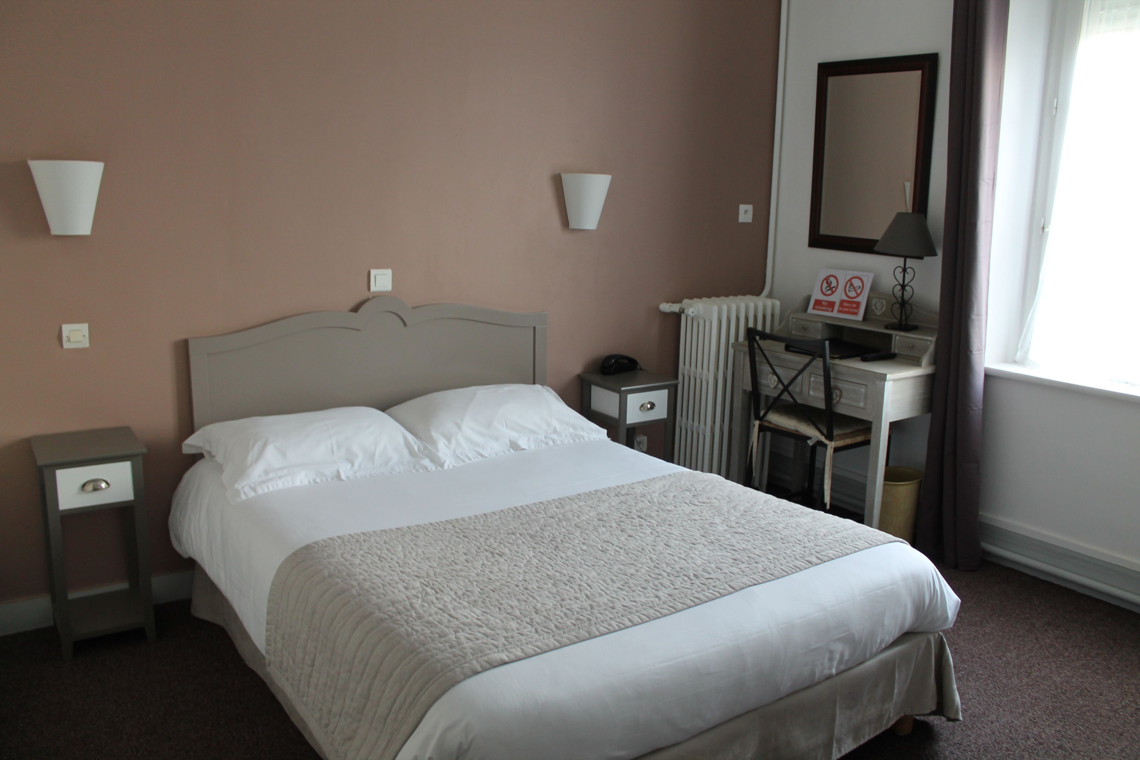 Een net opgemaakt bed in een hotelkamer, met een hoofdeinde, nachtkastjes, een bureau en een spiegel.