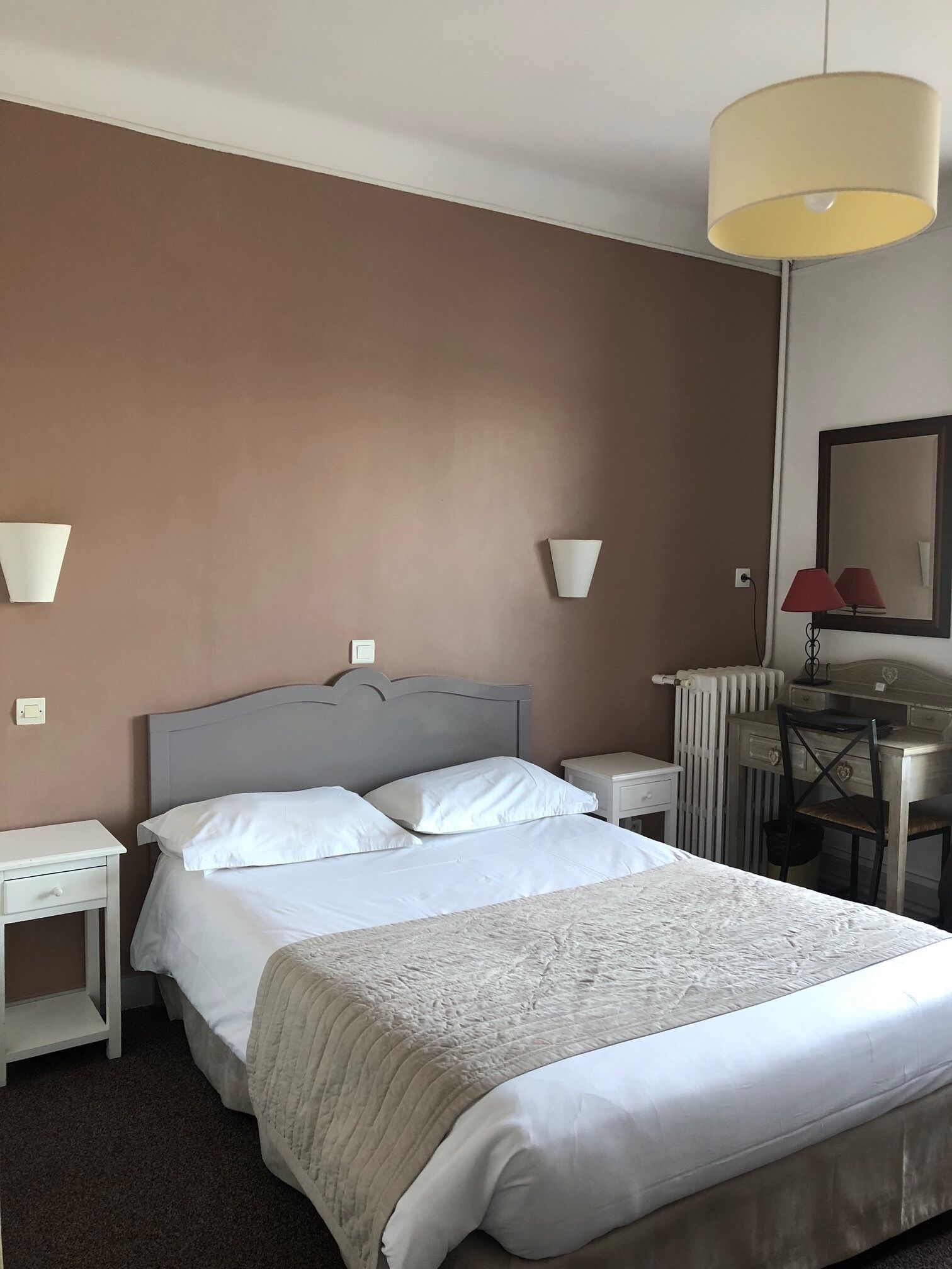 A hotel room with a bed, bedside tables, a desk, a chair, and a lamp.
