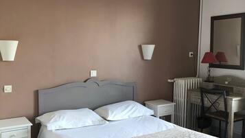 A hotel room with a bed, bedside tables, a desk, a chair, and a lamp.