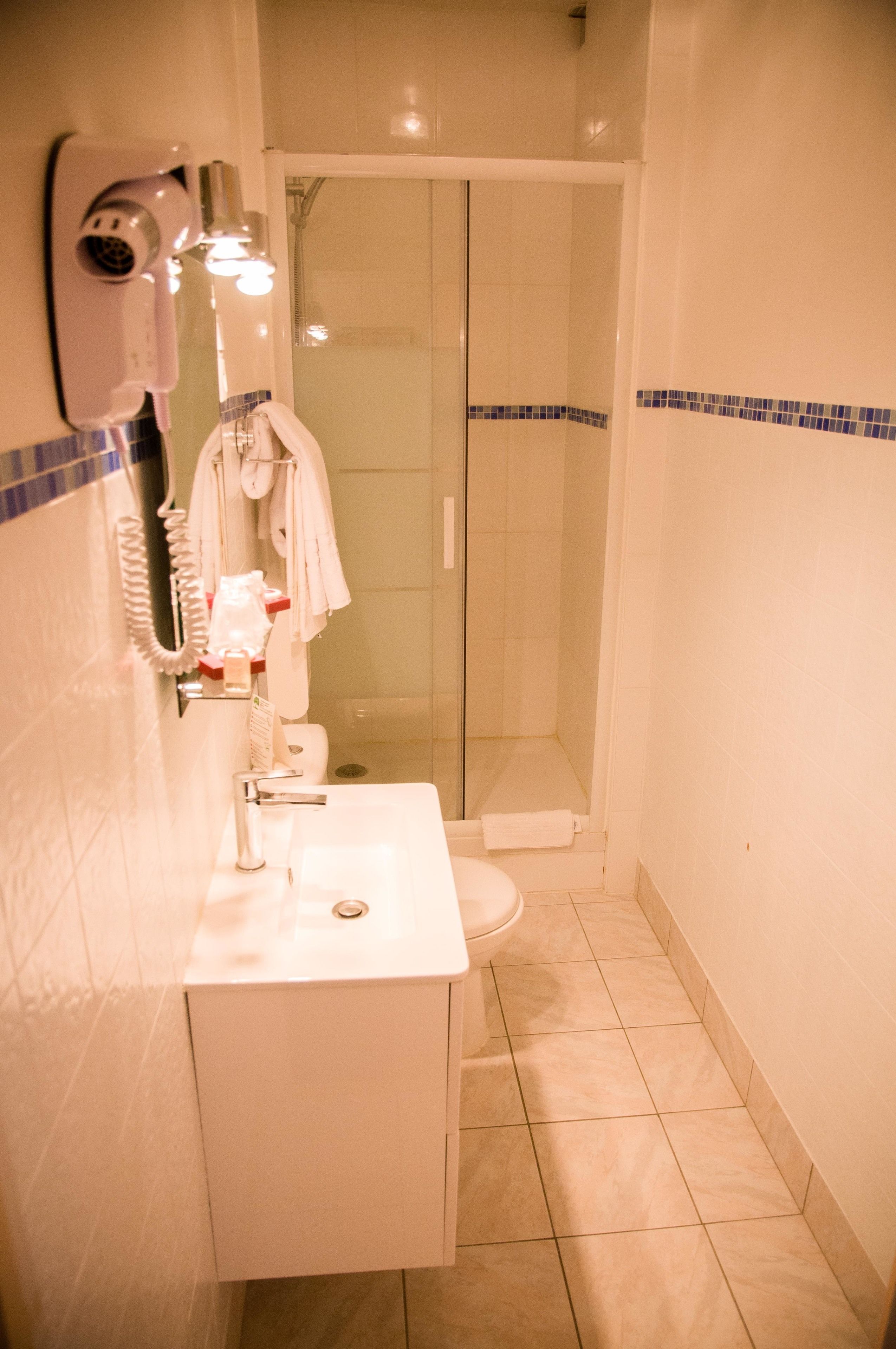 Une salle de bain avec un lavabo blanc, un sèche-cheveux et une douche à parois de verre.