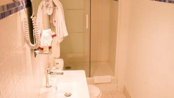 Une salle de bain avec un lavabo blanc, un sèche-cheveux et une douche à parois de verre.