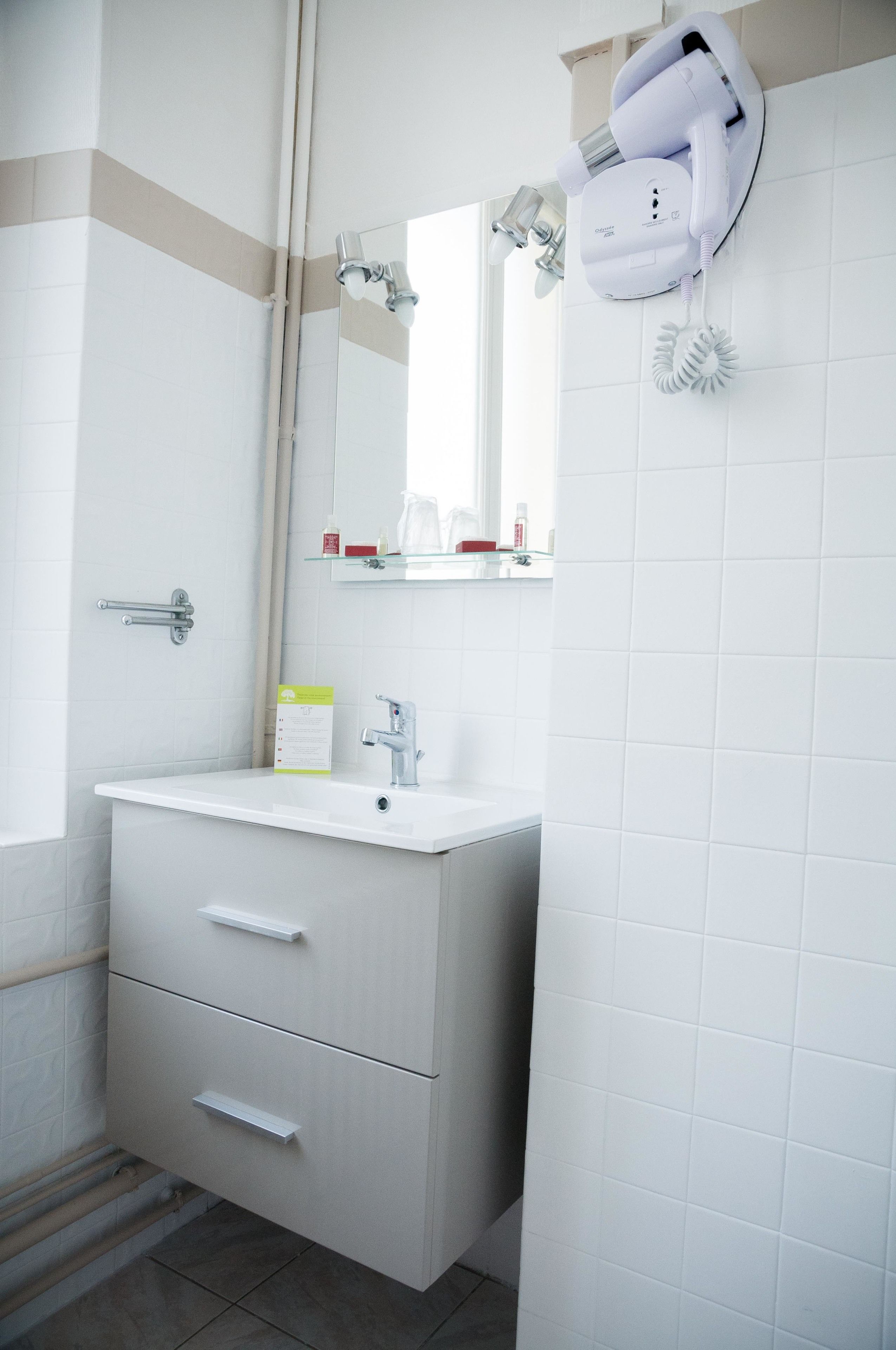 Un baño con lavamanos blanco, espejo y secador de pelo montado en la pared.