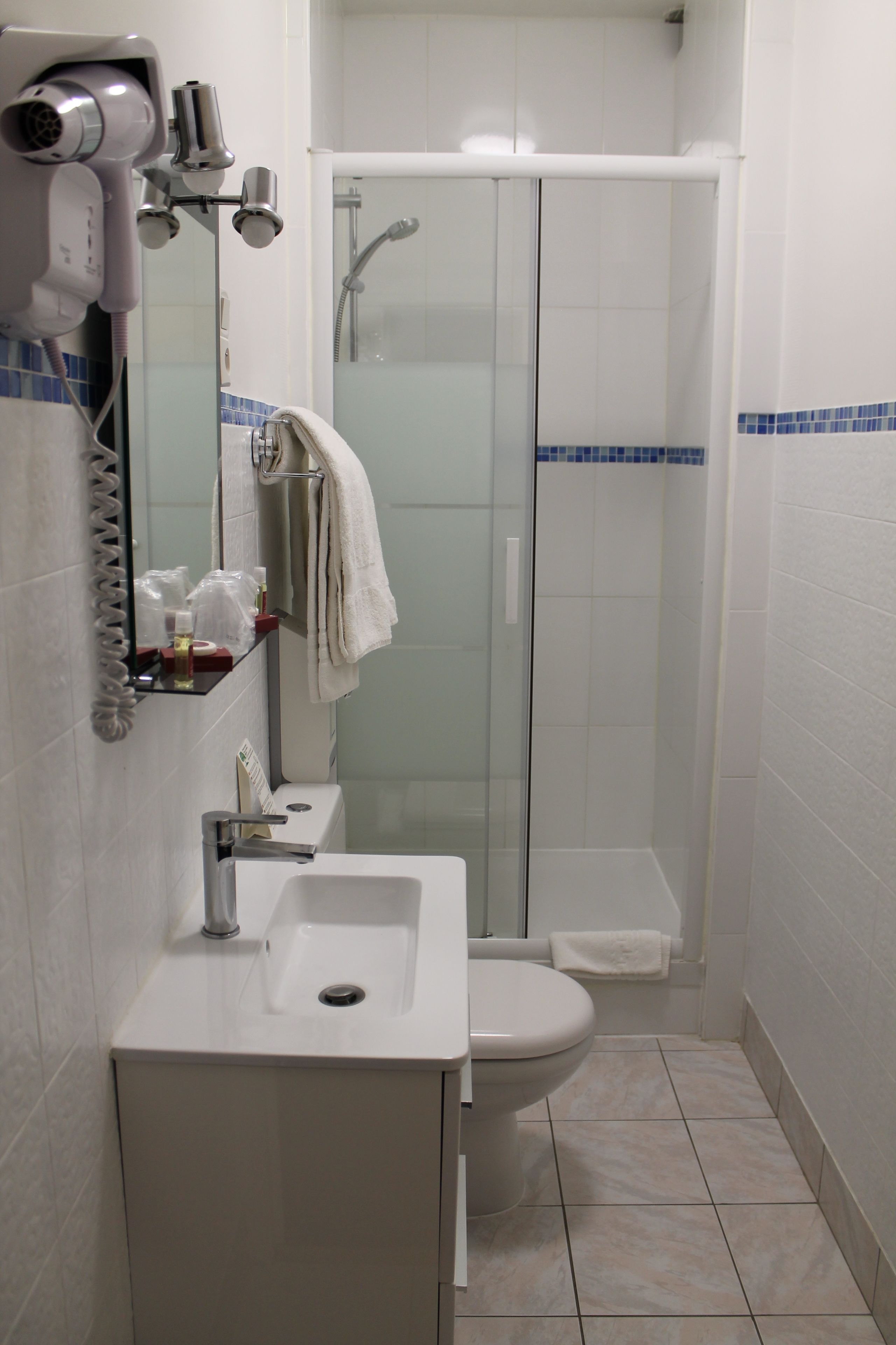 A bathroom with a white sink, toilet, and glass-enclosed shower. There is a hairdryer on the wall and a towel rack with a towel.