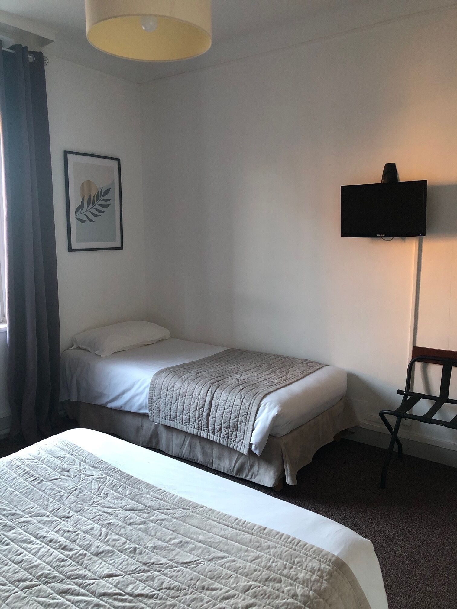 Una habitación de hotel con una cama, una silla, un televisor de pantalla plana y una obra de arte enmarcada en la pared.