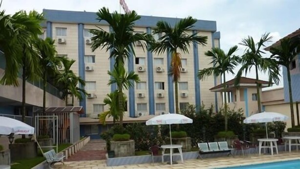 A hotel with a swimming pool, palm trees, and outdoor seating with umbrellas. - Somatel Hotel (Douala)