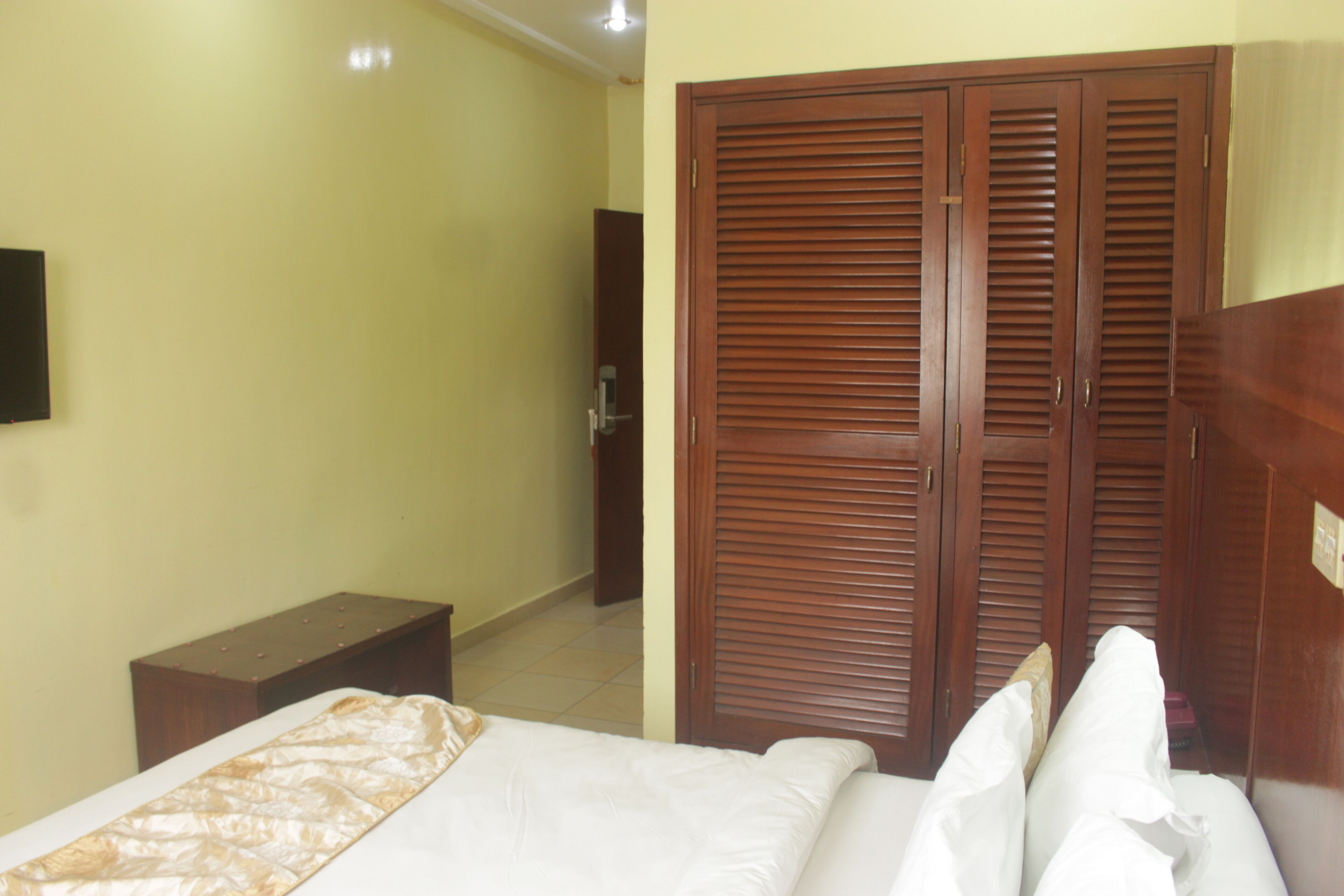 A bedroom with a bed, a wooden wardrobe, and a small bedside table.