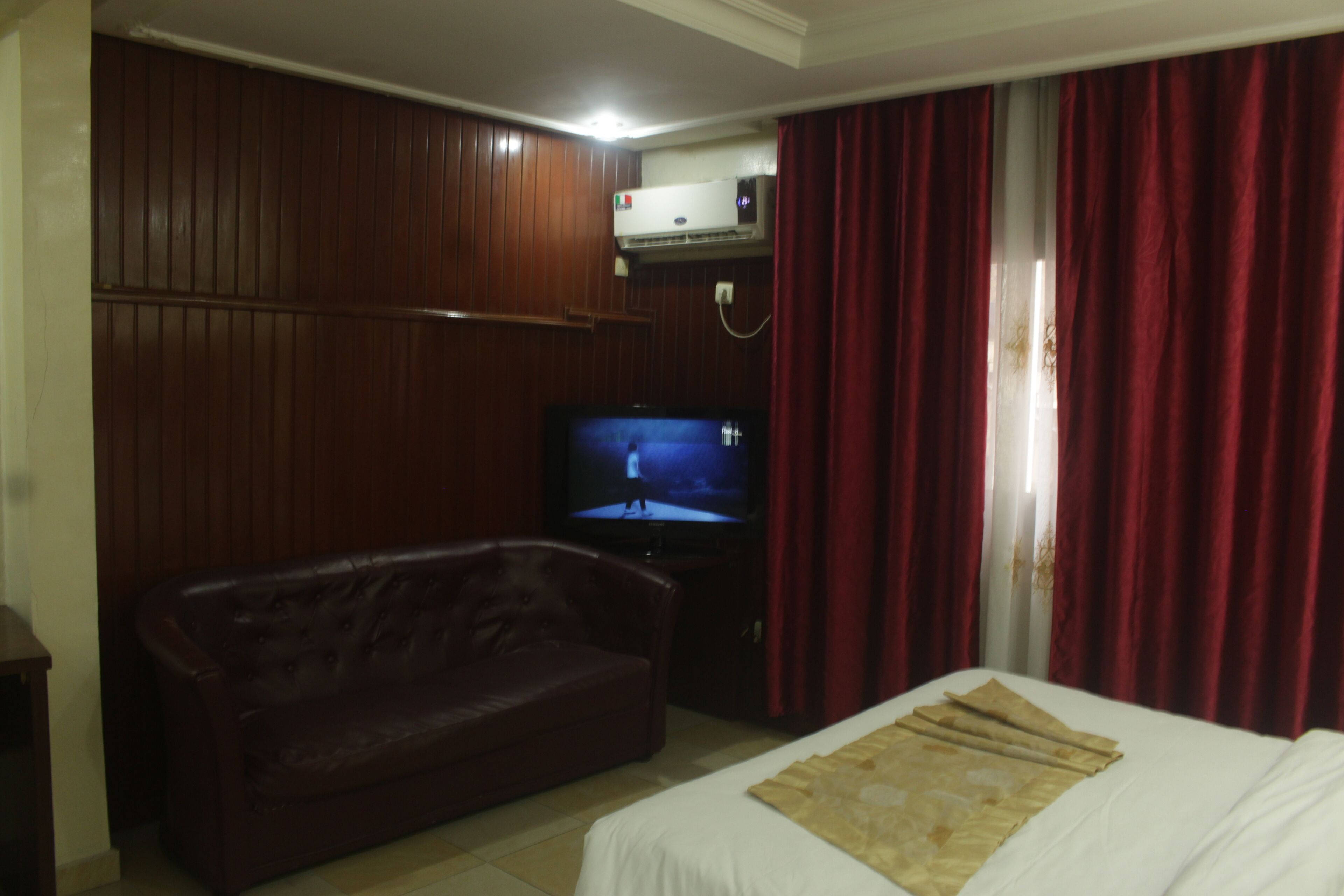 A hotel room with a bed, a television, a leather sofa, and wooden paneling on the walls.
