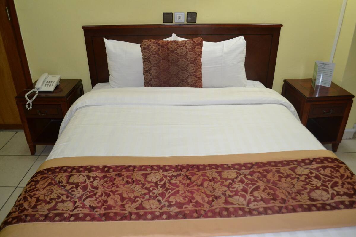 A hotel room with a large bed, two bedside tables, a telephone, and a sign indicating room amenities.