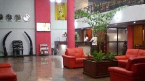Un hall con sofás rojos, un mostrador de recepción y una planta grande en maceta.