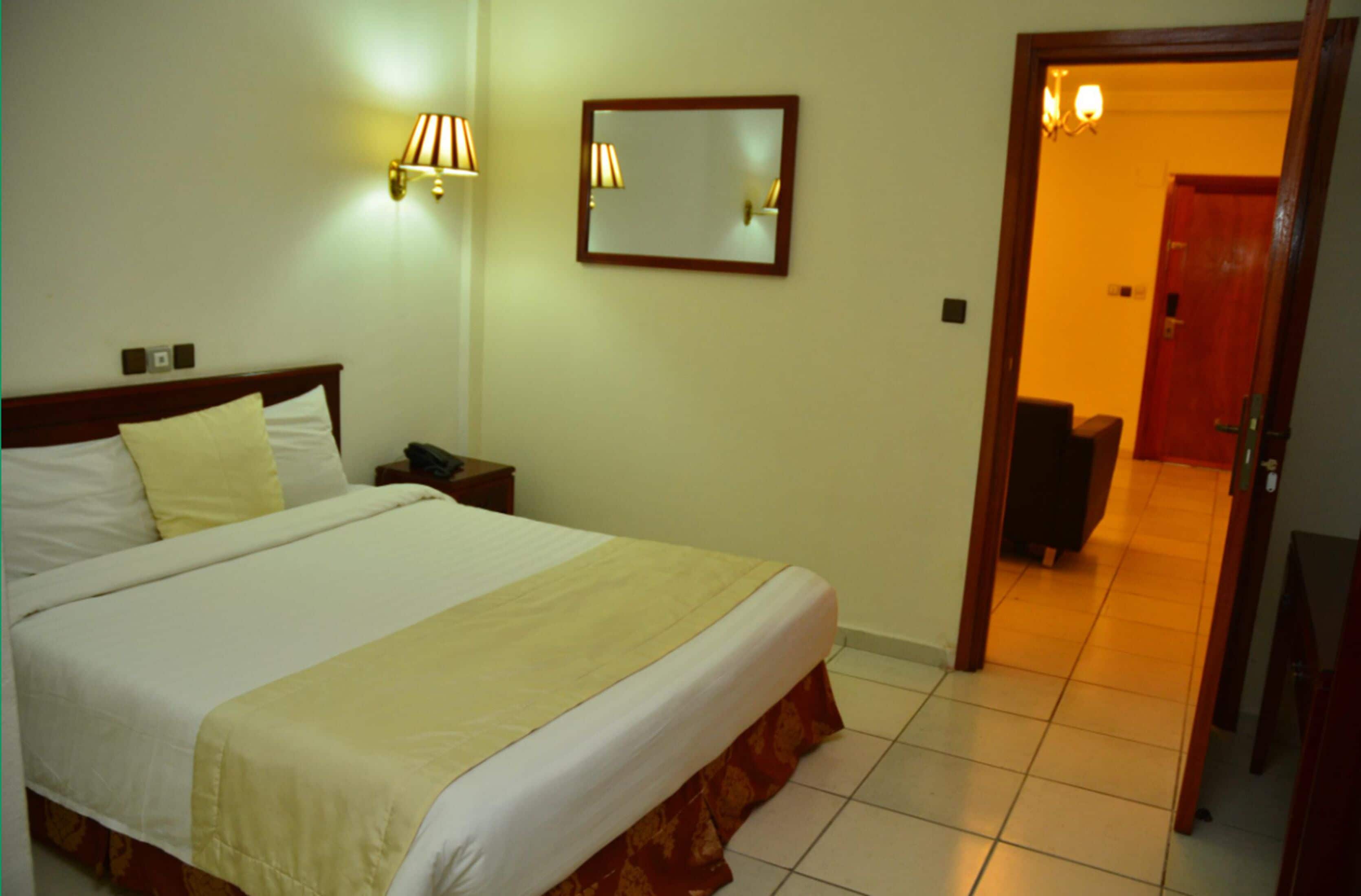 Una habitación de hotel con cama, lámpara de noche, mesita de noche y una puerta que da a otra habitación.