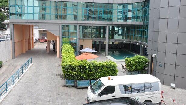 Un edificio moderno con fachada de vidrio, una zona de piscina y una furgoneta blanca estacionada frente a él.