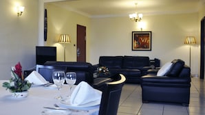 Un comedor con una mesa dispuesta para dos, un sofá de cuero negro y un cuadro en la pared.