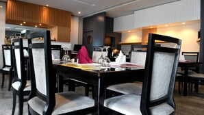 A modern dining area with a long table and multiple chairs, a bar area in the background, and a neutral color palette. - Planet Hotel (Douala)