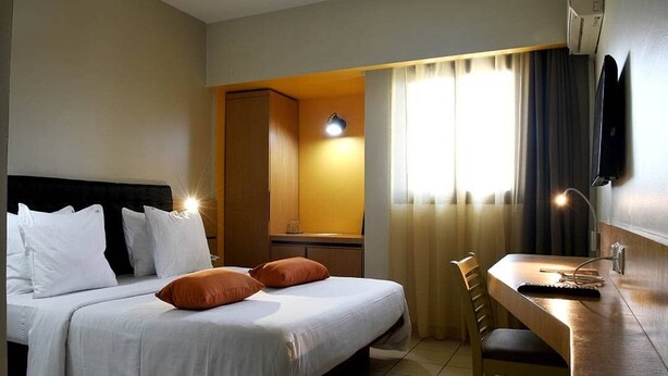 A hotel room with a bed, a desk, a chair, a wardrobe, and a window with curtains. - Planet Hotel (Douala)
