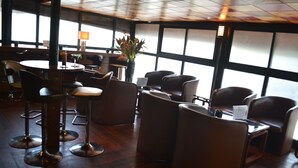 A modern restaurant with high tables and chairs, large windows, and a wooden floor. - Planet Hotel (Douala)