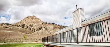 A building with a flat roof, a long covered walkway with black railings, and a stone hill in the background.