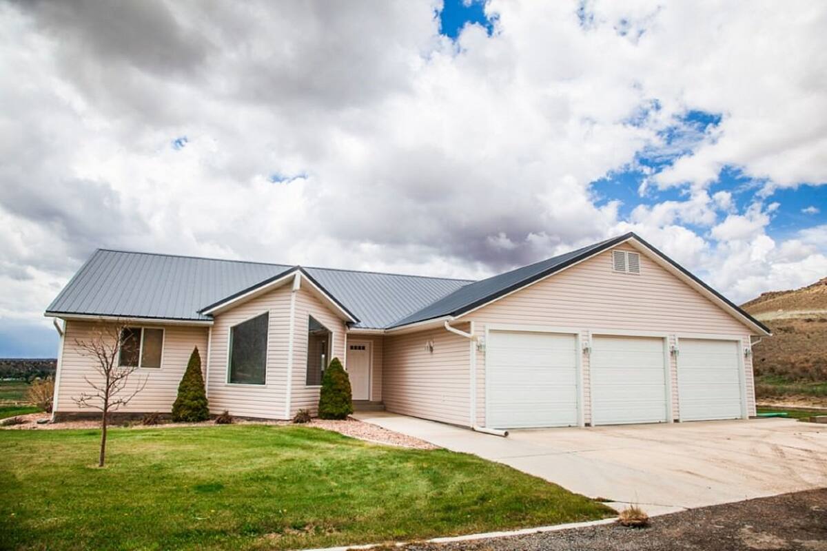 A two-story house with a garage, a small front yard, and a hilly landscape in the background.