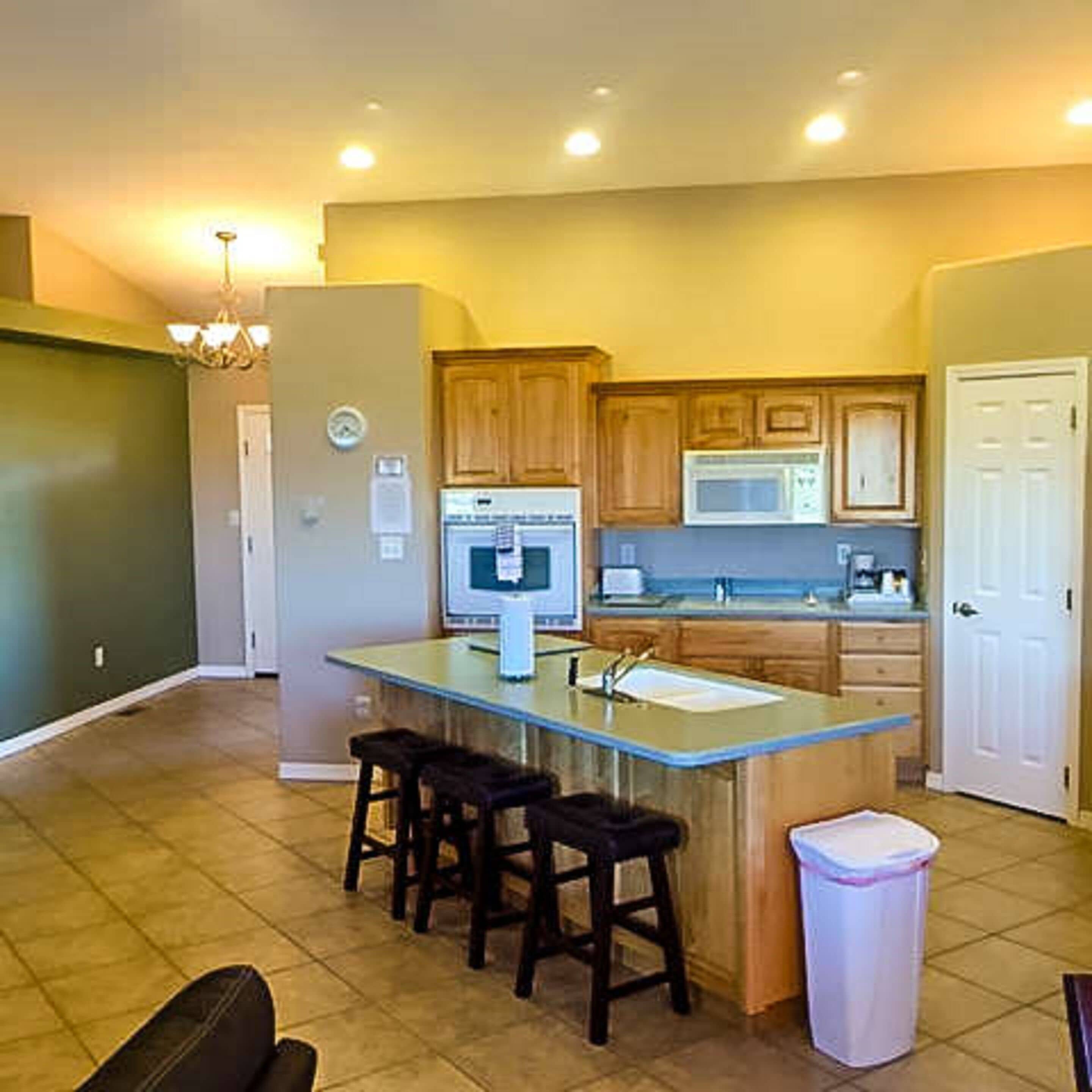 A compact kitchen with wooden cabinets, a microwave, a sink, and a small island with stools.