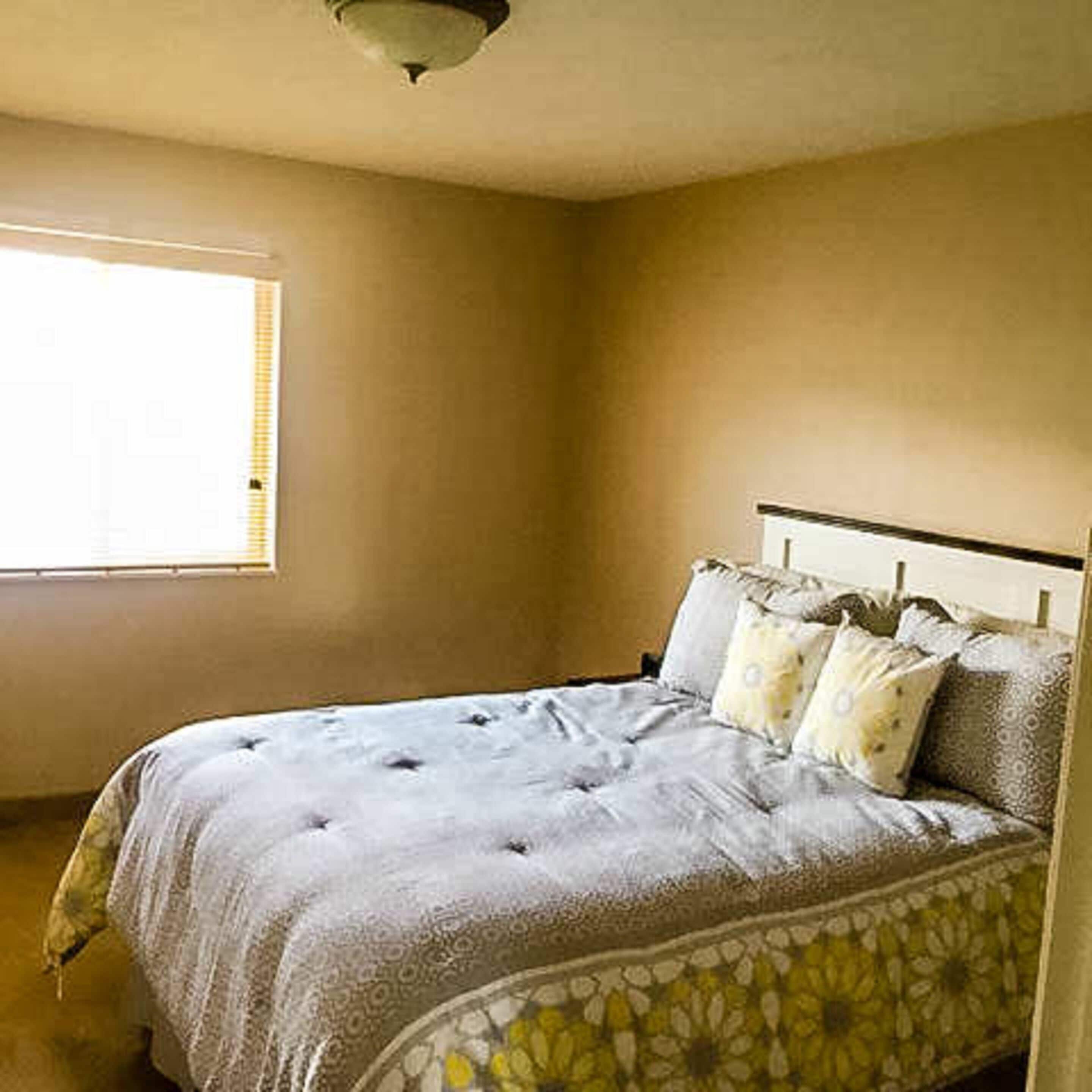A bedroom with a bed, a window, and a plain wall.