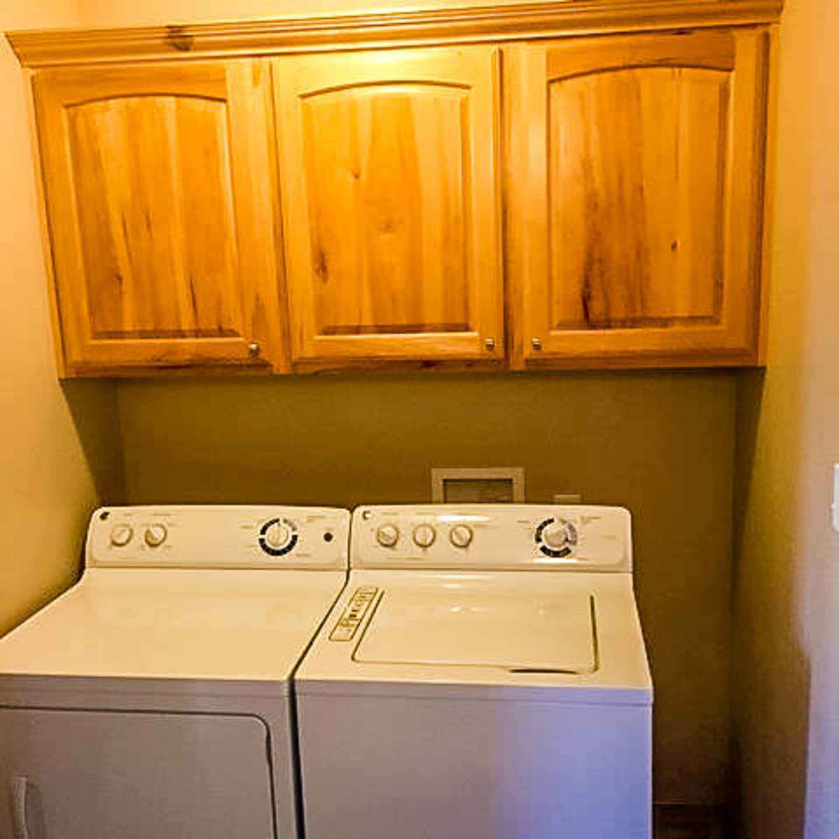 A laundry area with wooden cabinets above a white washer and dryer.