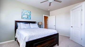 A bedroom with a bed, a ceiling fan, a door, and a painting on the wall.