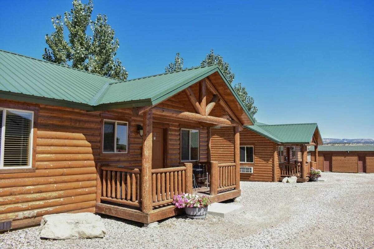 A log cabin with a porch, a covered outdoor seating area, and a gravel driveway.