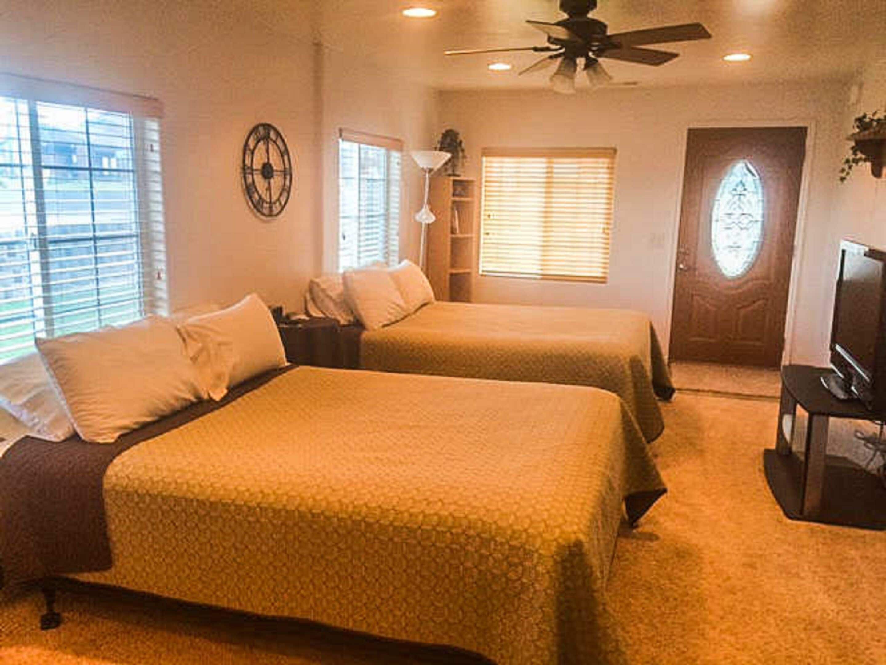 A hotel room with two beds, a ceiling fan, a TV, and a door with a window.