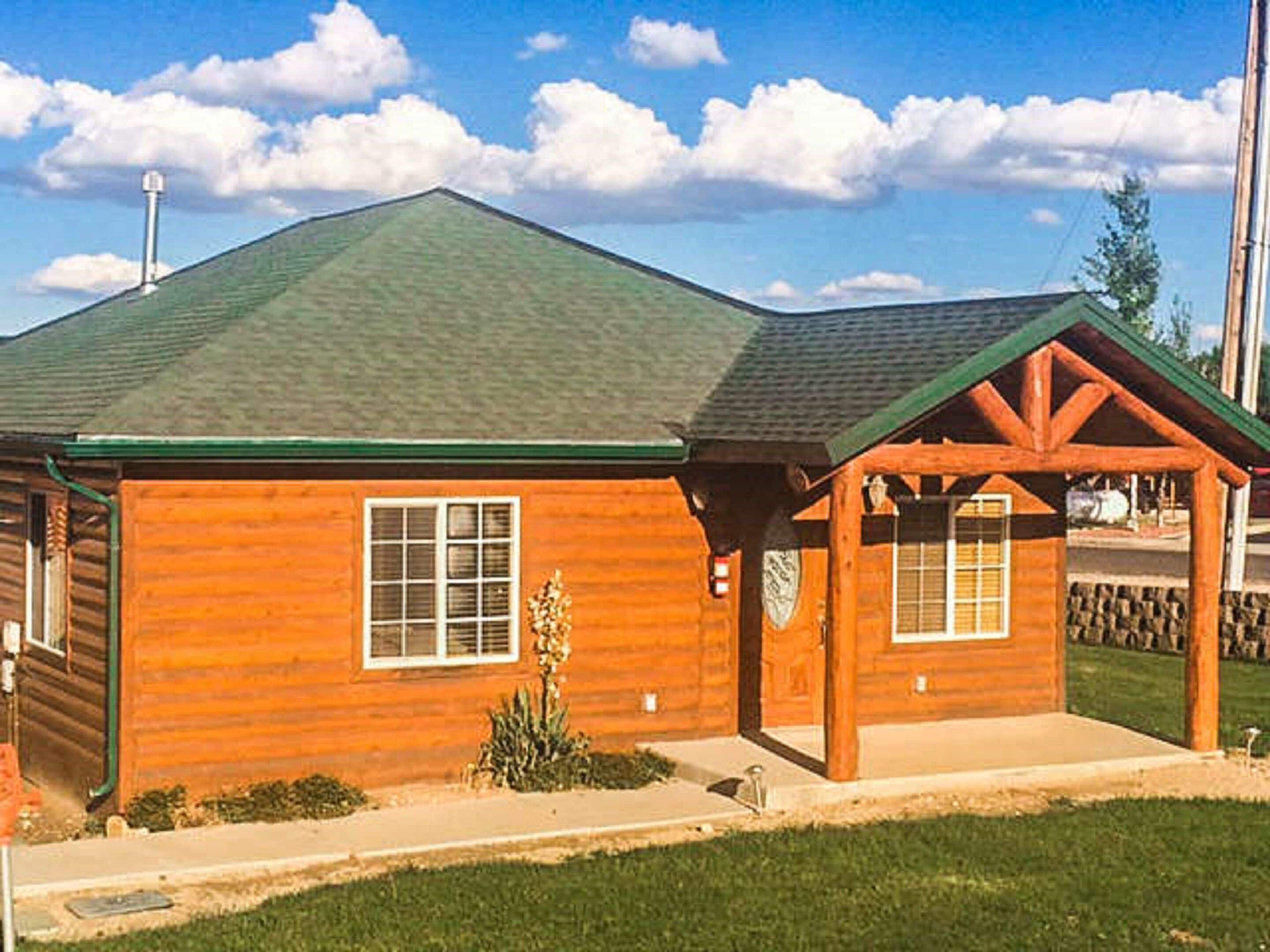 A wooden cabin with a green roof, a covered porch, and a small garden.