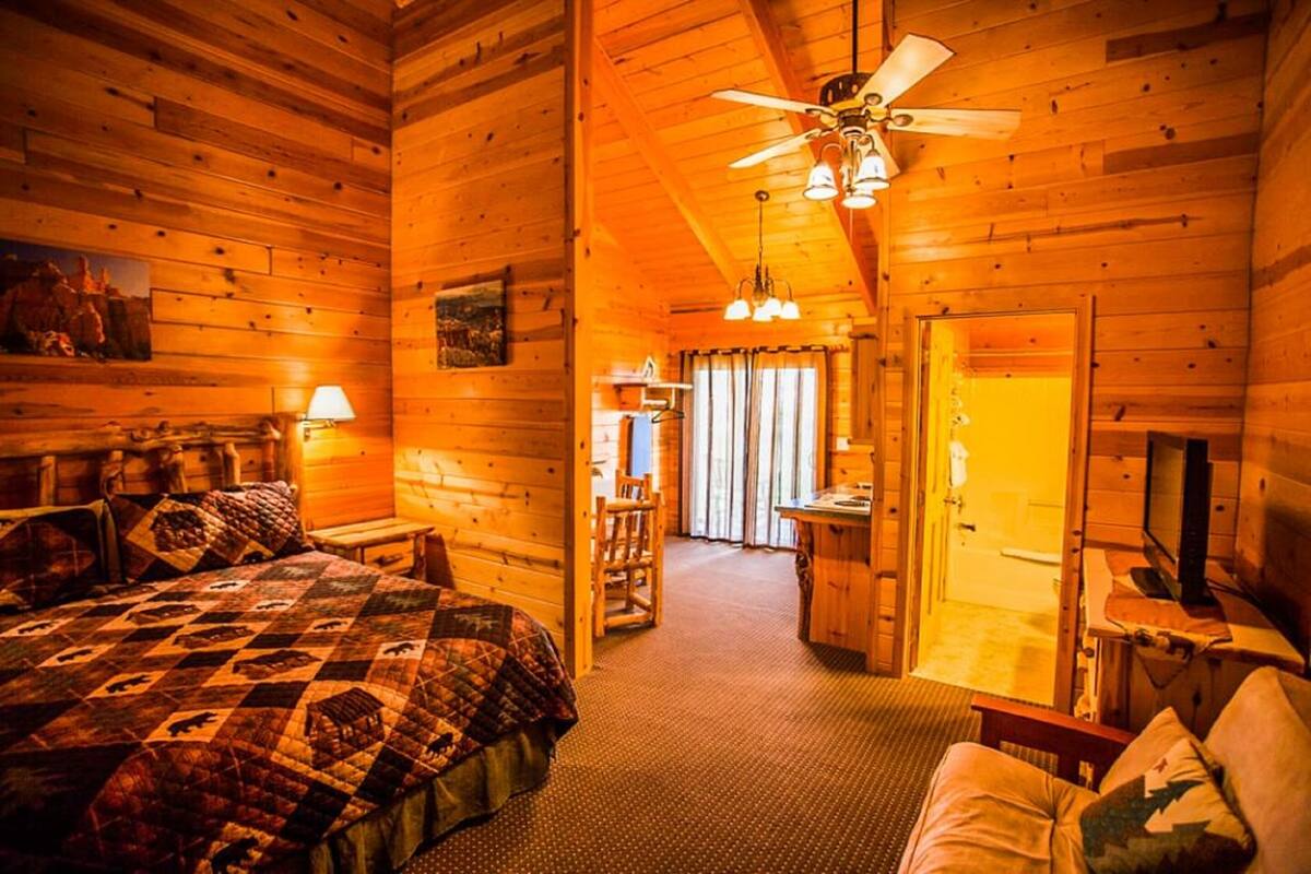 A cozy log cabin bedroom with a large bed, a ceiling fan, and a desk area.