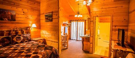 A cozy log cabin bedroom with a large bed, a ceiling fan, and a desk area.