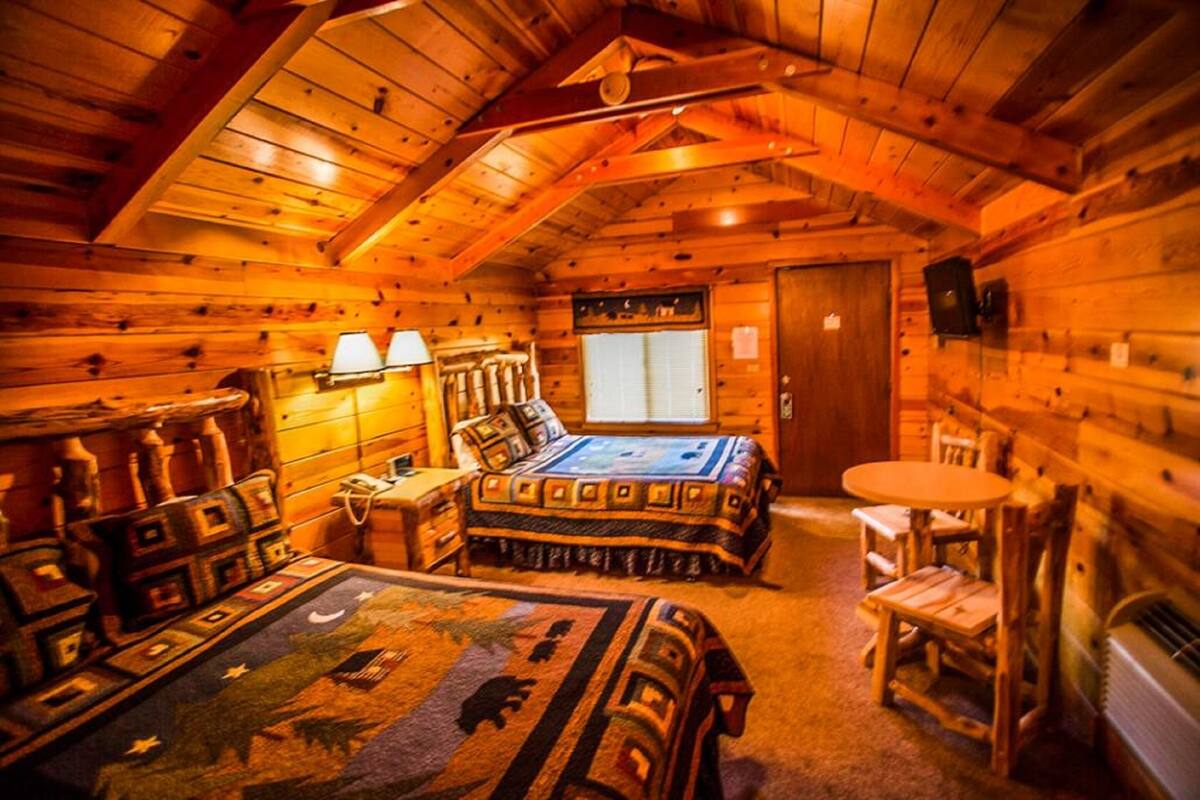 A log cabin room with a bed, a small table, and a chair.