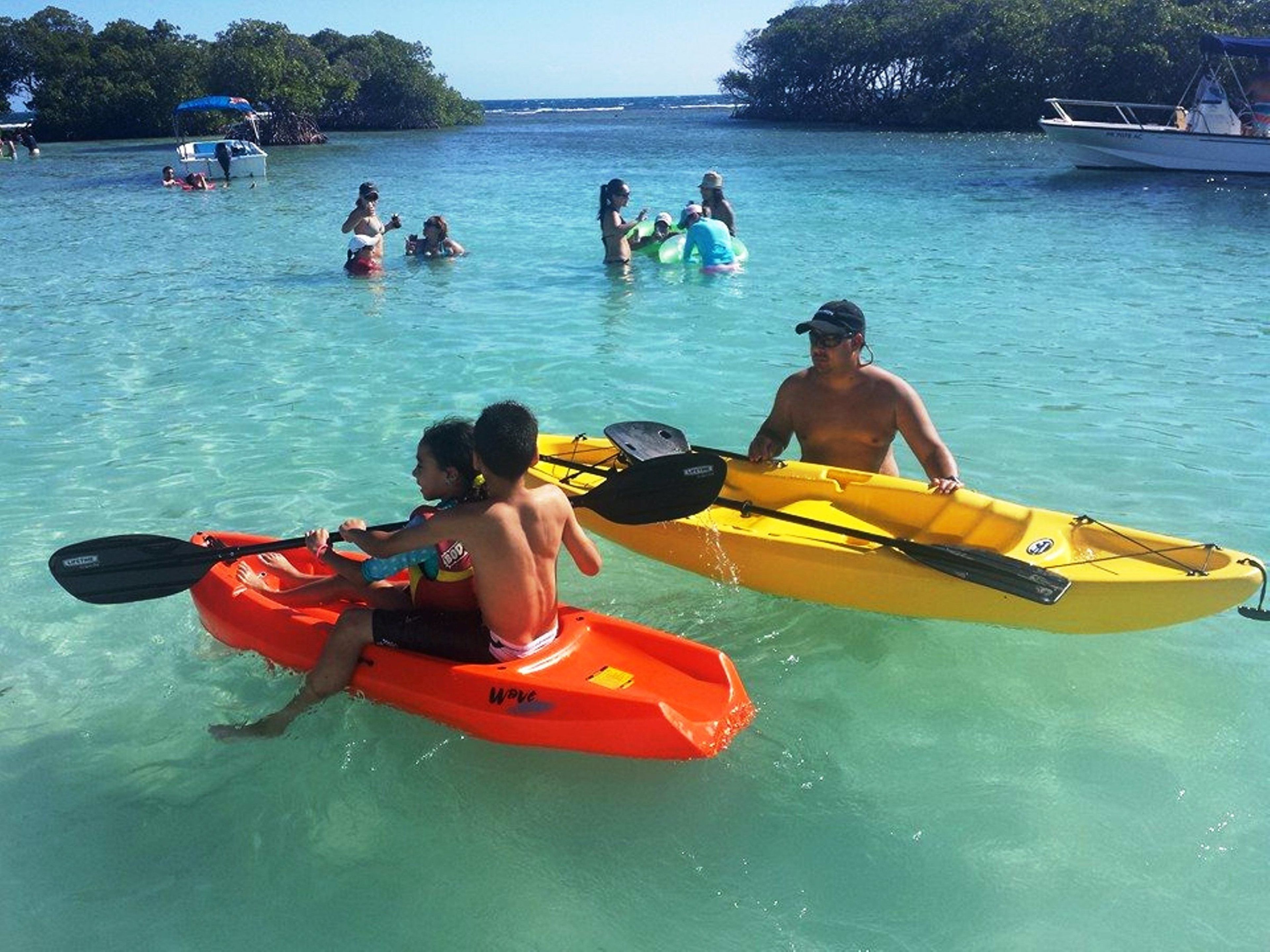 A group of people in kayaks and a boat on a clear blue sea.