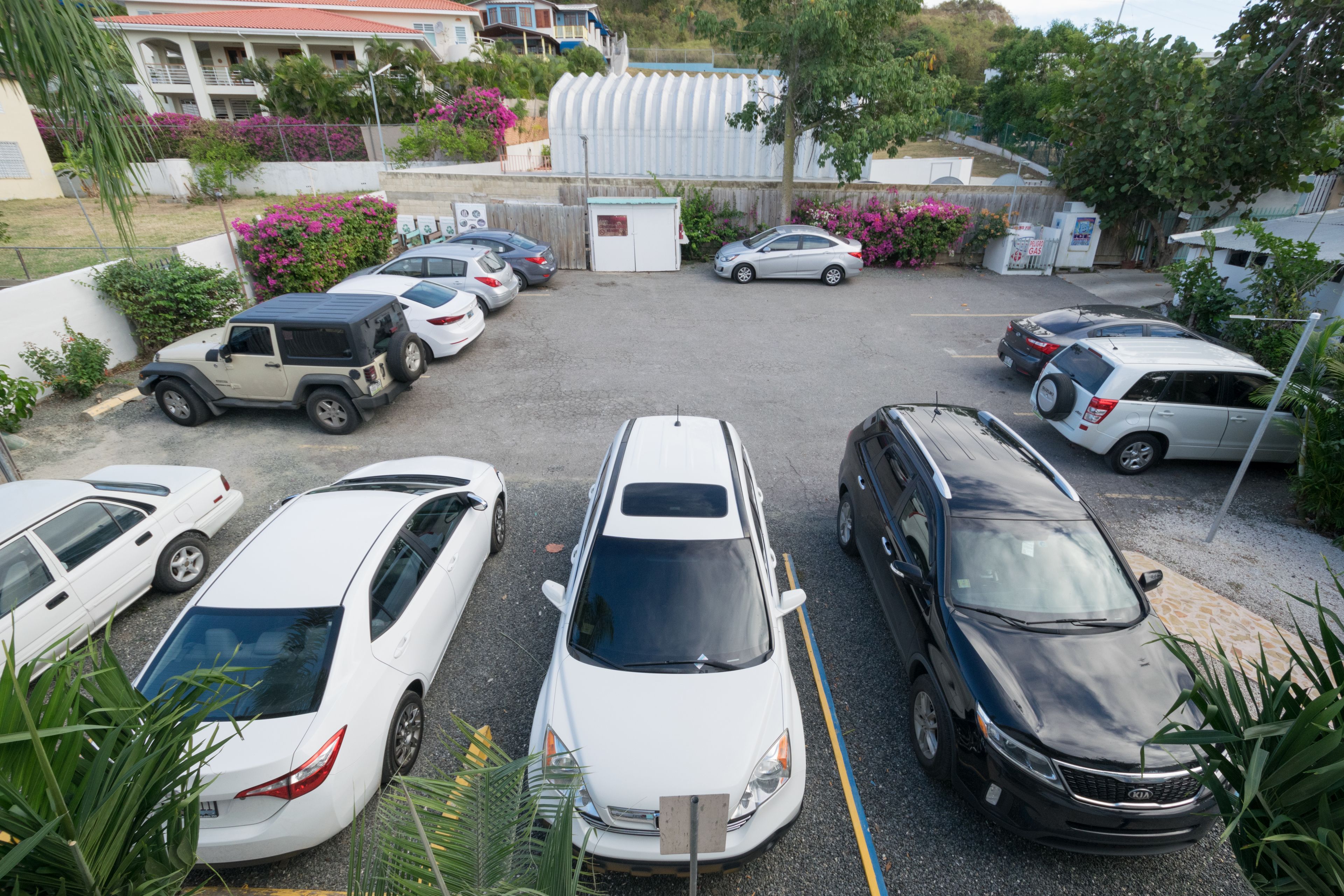 A parking lot with several cars, including a white sedan, a black SUV, and a silver sedan.