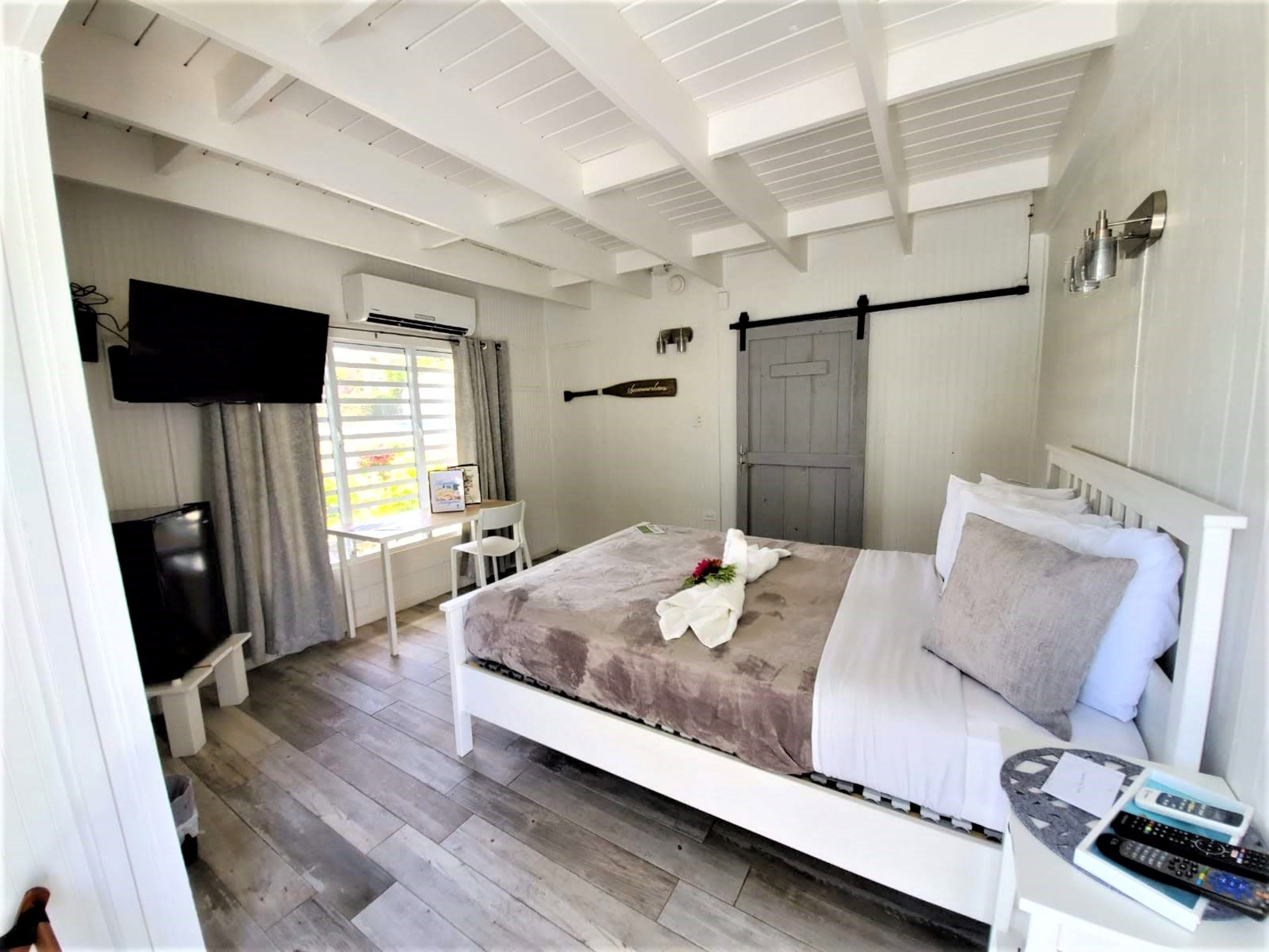 A bedroom with a bed, a desk, a chair, a TV, and a door.