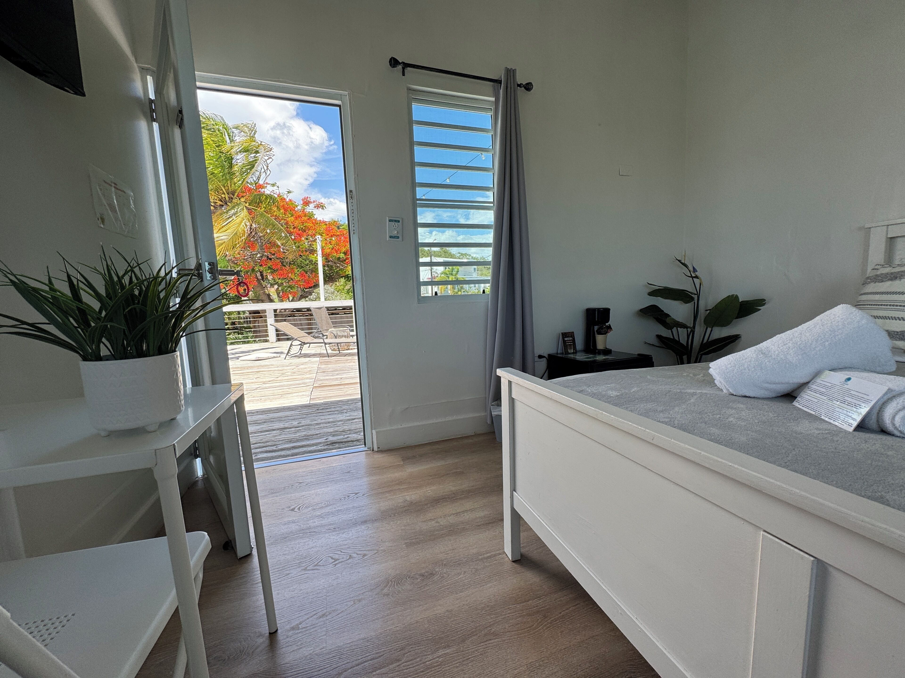 A bedroom with a bed, a desk, a potted plant, and a view of the outdoors.