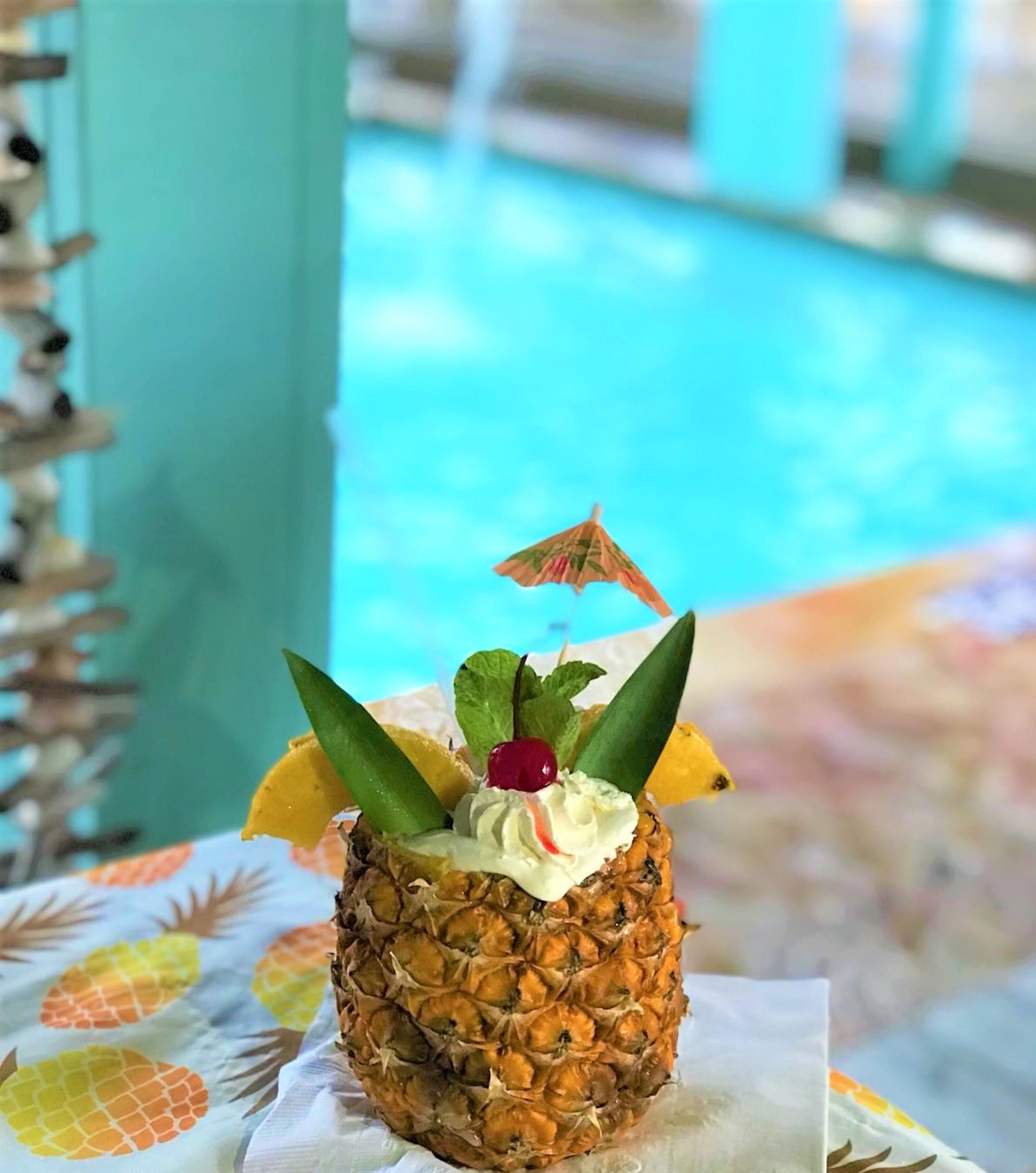 A pineapple dessert on a table with a pool in the background.