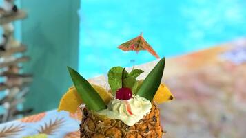 A pineapple dessert on a table with a pool in the background.
